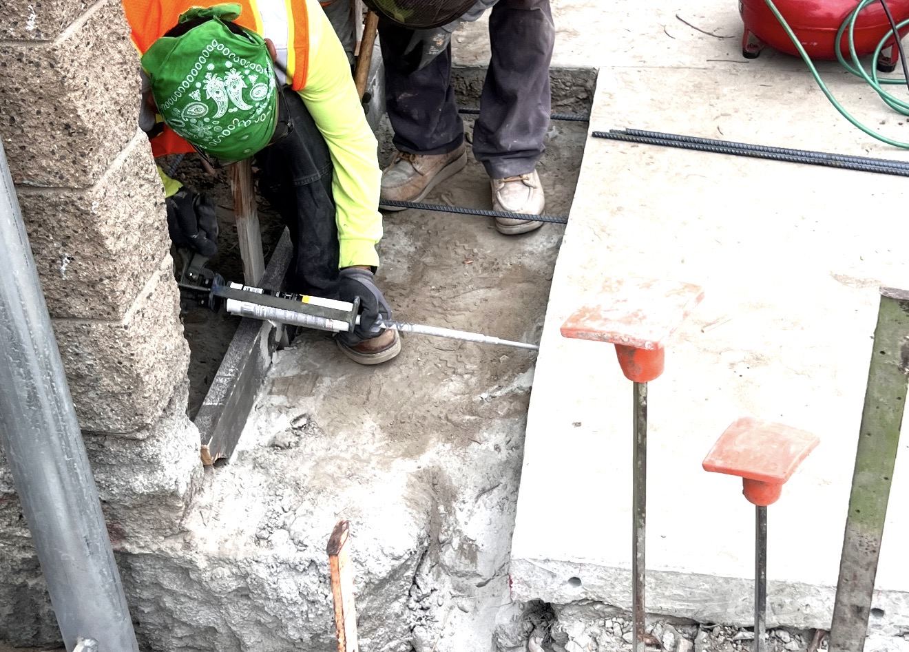 Worker injecting epoxy adhesive into drilled holes for rebar dowels